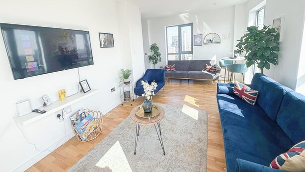 En moderne stue med et fladskærms-tv, en blå sofa, et sofabord og et stort vindue der lukker naturligt lys ind.
