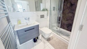 Et moderne badeværelse med et glasbadeværelse, et hvidt toilet og en vaskebord med marmorplade.