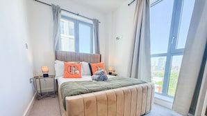 Ein Schlafzimmer mit einem großen Bett, einem Nachttisch, einer Lampe und Blick auf die Stadt durch große Fenster.