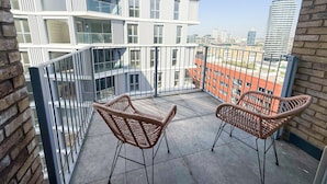 Ein Balkon mit Korbstühlen, Blick auf eine Stadtlandschaft und ein modernes Gebäude mit Balkonen.