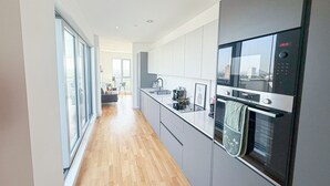 Eine moderne Küche mit Einbauofen, Mikrowelle und Kühlschrank. Durch die Glastüren ist ein Essbereich mit Tisch und Stühlen zu sehen.
