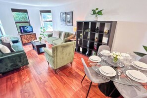 A modern living room with a sofa, a dining table set for four, and a bookshelf.