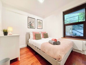 A bedroom with a bed, a bedside table with a lamp, a window with a view, and a radiator.