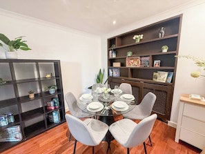 A dining area with a round glass table set for six, surrounded by grey upholstered chairs.