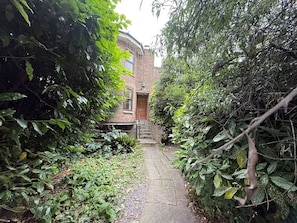 A narrow stone pathway leading to a brick building with a door and steps.