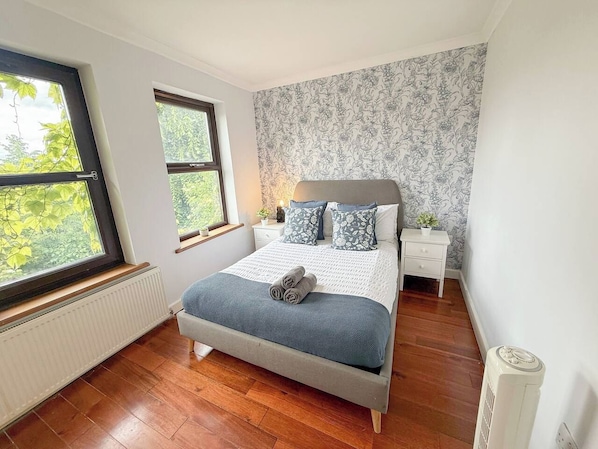 A bedroom with a bed, a nightstand, a radiator, and a window with a view of trees.