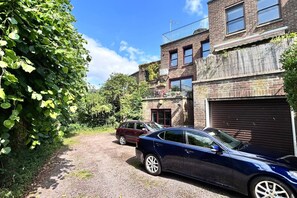 A residential street with two parked cars, a brick building with a garage, and a tree-lined path. - New 4-bed Home in Crouch End near alexandra palace (London)