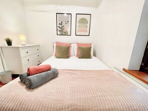 A bedroom with a bed, pillows, a bedside table with a lamp, a small plant, and artwork on the wall. - New 4-bed Home in Crouch End near alexandra palace (London)