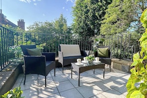An outdoor patio with wicker furniture, a glass table, and a metal fence.