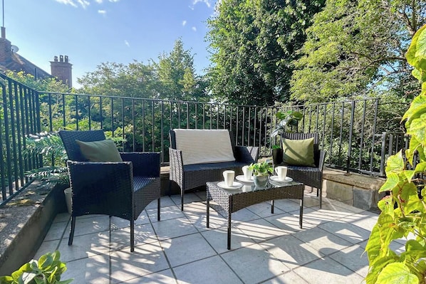 An outdoor patio with wicker furniture, a glass table, and a metal fence.