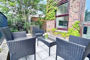 An outdoor seating area with wicker furniture and a glass table, surrounded by a brick building with ivy. - New 4-bed Home in Crouch End near alexandra palace (London)
