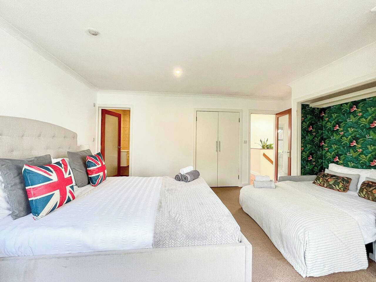 A hotel room with two beds, a wardrobe, a door leading to a bathroom, and a green wallpapered wall.