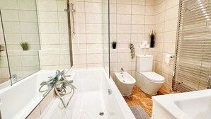 Et stilfuldt badeværelse med et stort badekar, en bidet, et toilet og en brusekabine i glas.