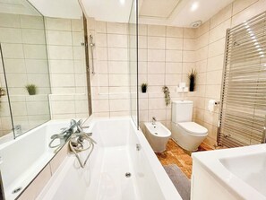 Uma casa de banho moderna com uma banheira grande, um bidé, uma sanita e cabine de duche em vidro.