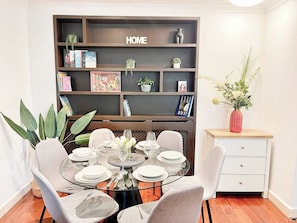 A dining area with a glass table set for four, surrounded by chairs. A bookshelf with the word 'HOME' is behind the table. - New 4-bed Home in Crouch End near alexandra palace (London)