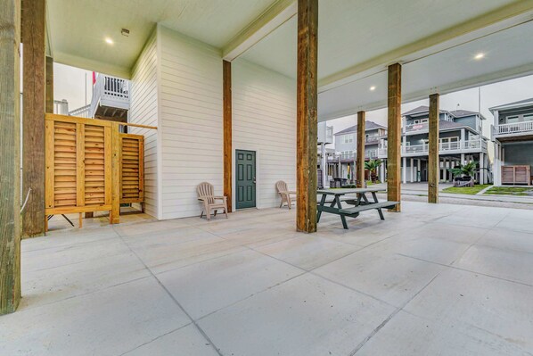 A covered outdoor area with a picnic table and two Adirondack chairs, wooden shutters, and a green door.