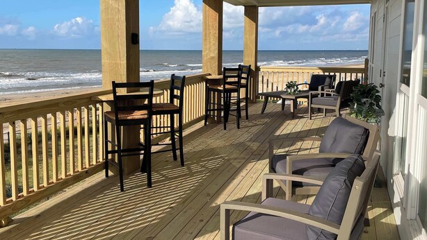 Een overdekt terras met houten vloer, buitenmeubilair en uitzicht op de oceaan.