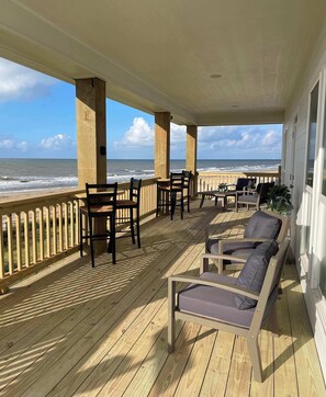 A covered deck with wooden flooring, outdoor furniture, and a view of the ocean.