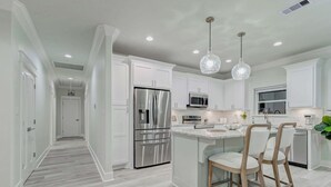 Een moderne keuken met witte kasten, roestvrijstalen apparatuur en een centraal eiland met barstoelen.