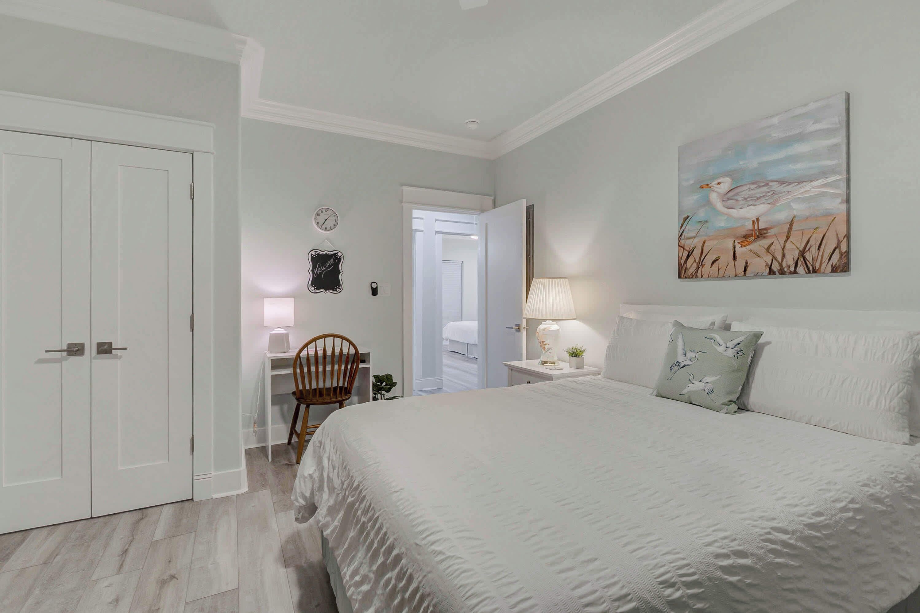Une chambre avec un grand lit, une chaise, un bureau et un tableau accroché au mur.