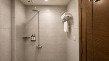 A modern shower with a handheld showerhead, a towel rack with folded towels, and a shelf with toiletries.
