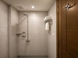 A modern shower with a handheld showerhead, a towel rack with folded towels, and a shelf with toiletries.