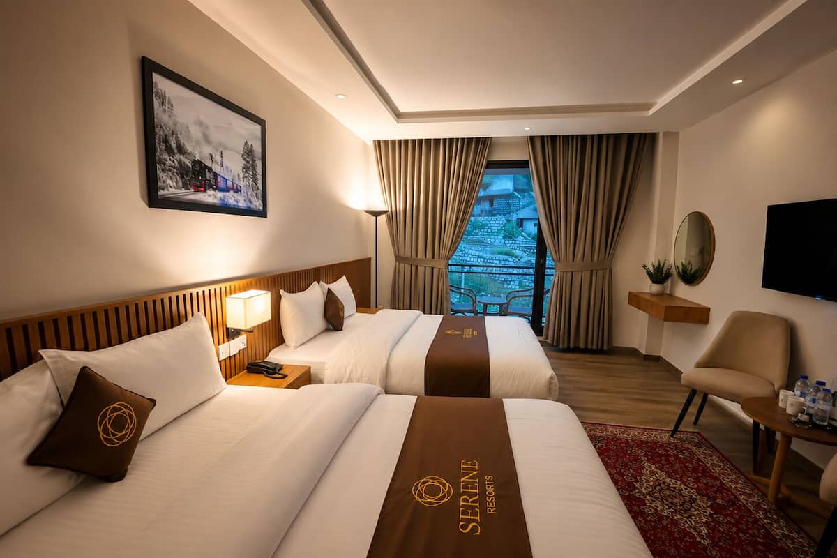 A hotel room with two beds, a TV, a desk, and a view of a mountainous landscape.