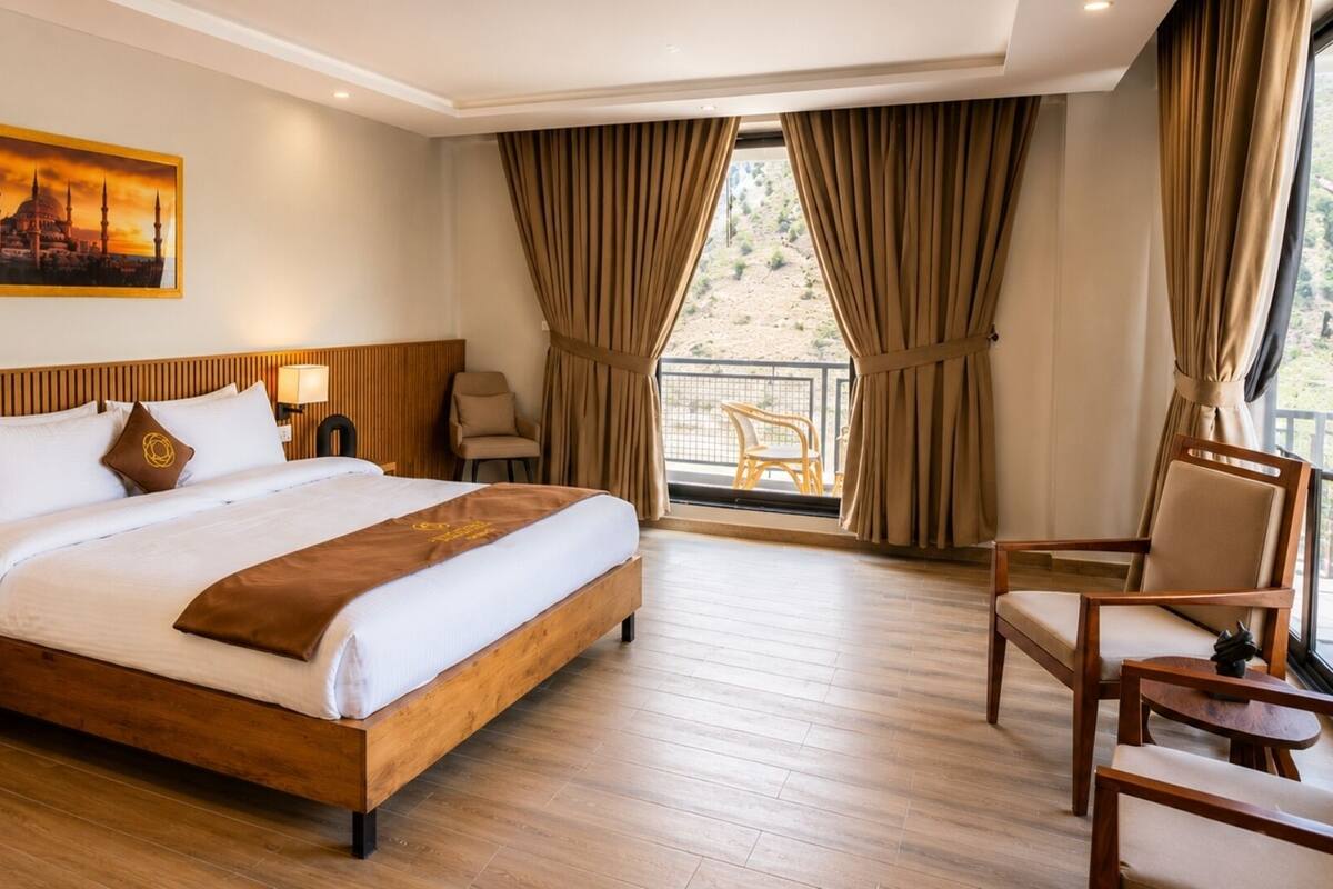 A hotel room with a wooden bed, nightstands, a chair, and a view of the outdoors.