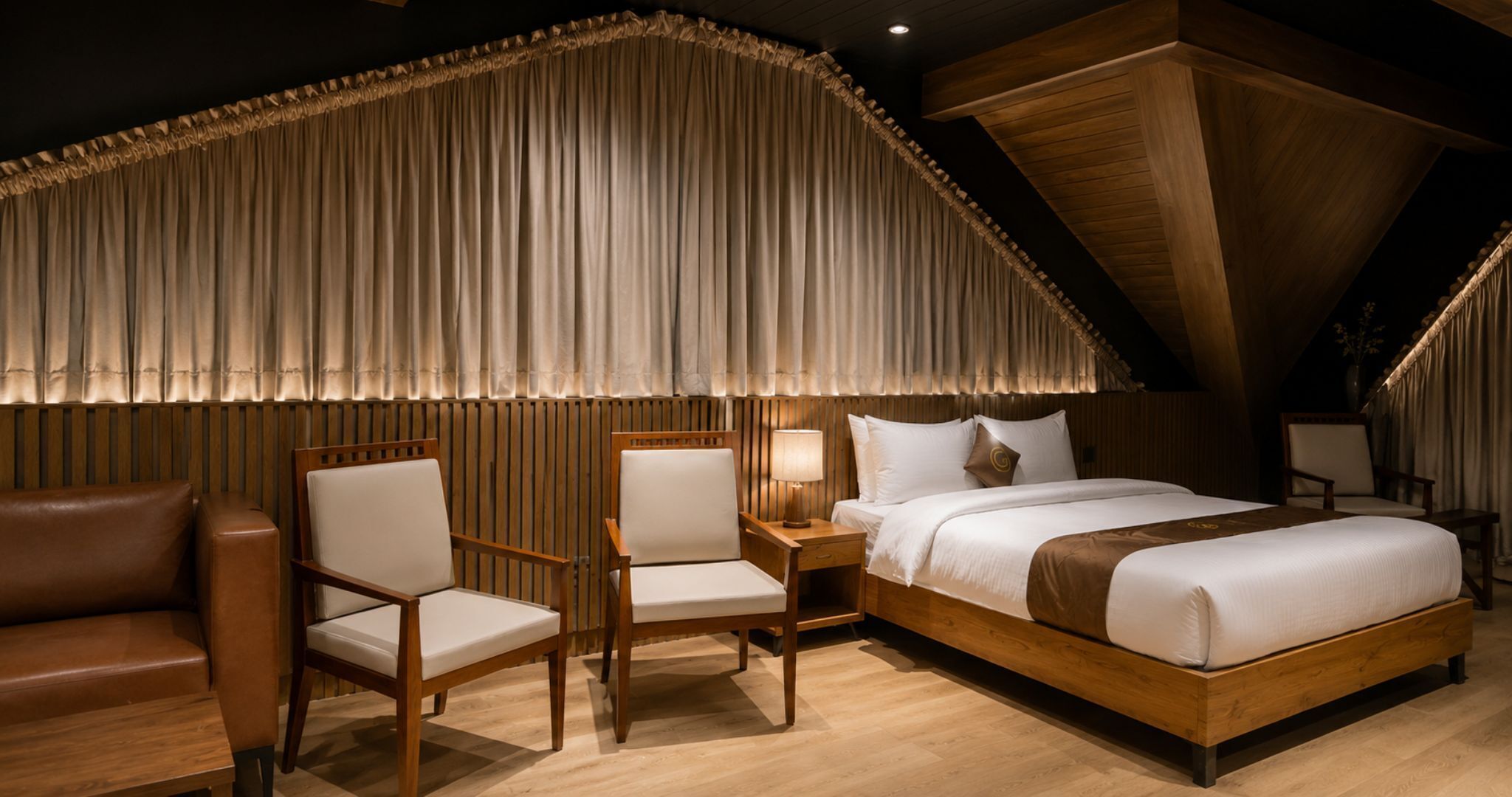 Une chambre d’hôtel avec un grand lit, deux fauteuils, une tête de lit en bois et un plafond orné de lattes en bois.