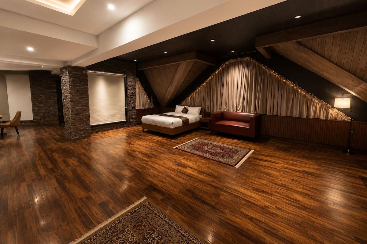 A bedroom with a sloped ceiling, wooden flooring, a bed, a red sofa, and a large window with curtains.
