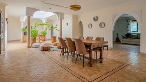 Un vaste espace dédié à la salle à manger, avec une table et des chaises en bois, entouré de plantes en pot et agrémenté d’un tapis à motifs.