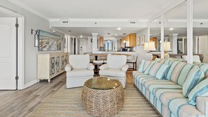 A spacious living room with a sofa, chairs, and a coffee table. A kitchen is visible in the background.