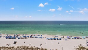 A beach with rows of sun umbrellas and beach chairs, a lifeguard tower, and the ocean in the background.