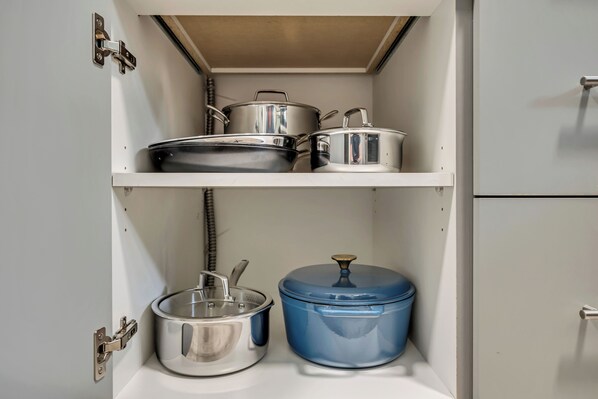 A kitchen cabinet with stainless steel pots and a blue pot on the shelves.