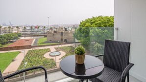 A balcony with a round table and wicker chairs, overlooking a cityscape with a garden and a historic building.