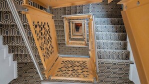 Spiraalimainen portaikko, jonka seinissä on geometriset kuviot, ja seinässä on punainen palosammutin.