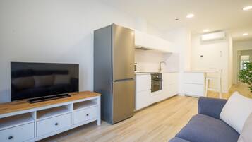 A modern living room with a flat-screen TV, a sofa, and a kitchen area with a refrigerator and oven.
