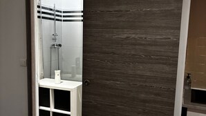 Une salle de bain moderne avec une douche, un lavabo blanc et une porte en bois.