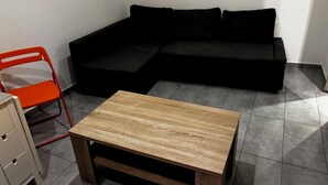 Un salon moderne avec un canapé d’angle, une petite table basse en bois et une chaise pliante rouge.