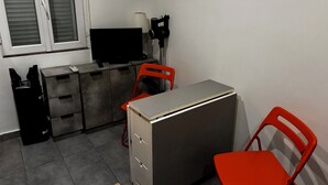 Une pièce de taille modeste, comprenant un bureau, deux chaises rouges, un téléviseur, une lampe et un petit meuble.