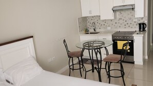A bedroom with a bed, a small dining table with chairs, and a kitchenette with a stove and sink. - Scenic studio in Portmore, Jamaica (Kingston)