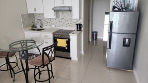 A modern kitchen with white cabinets, a gas stove, a stainless steel refrigerator, and a glass dining table with chairs. - Scenic studio in Portmore, Jamaica (Kingston)