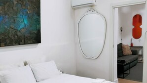 Une chambre d’hôtel avec un grand lit, un miroir rond, une petite table avec un livre, et un tableau abstrait rouge accroché au mur.