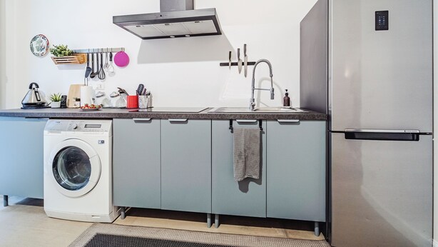 Une cuisine compacte dotée d’un lave-linge, d’appareils électroménagers en acier inoxydable et d’un design moderne.