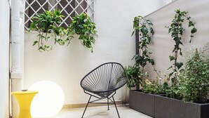Un coin avec une chaise à armature métallique noire, un tabouret jaune et des plantes en pot, le tout adossé à un mur blanc.