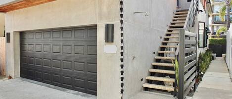A modern two-story house with a garage, a staircase with a railing, and a small garden area.