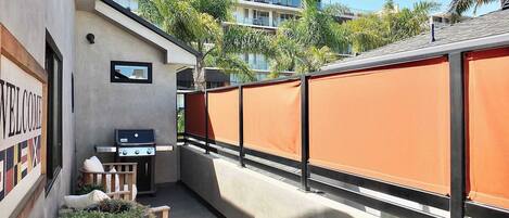 A balcony with a barbecue grill, a welcome sign, and a view of a multi-story building with balconies.