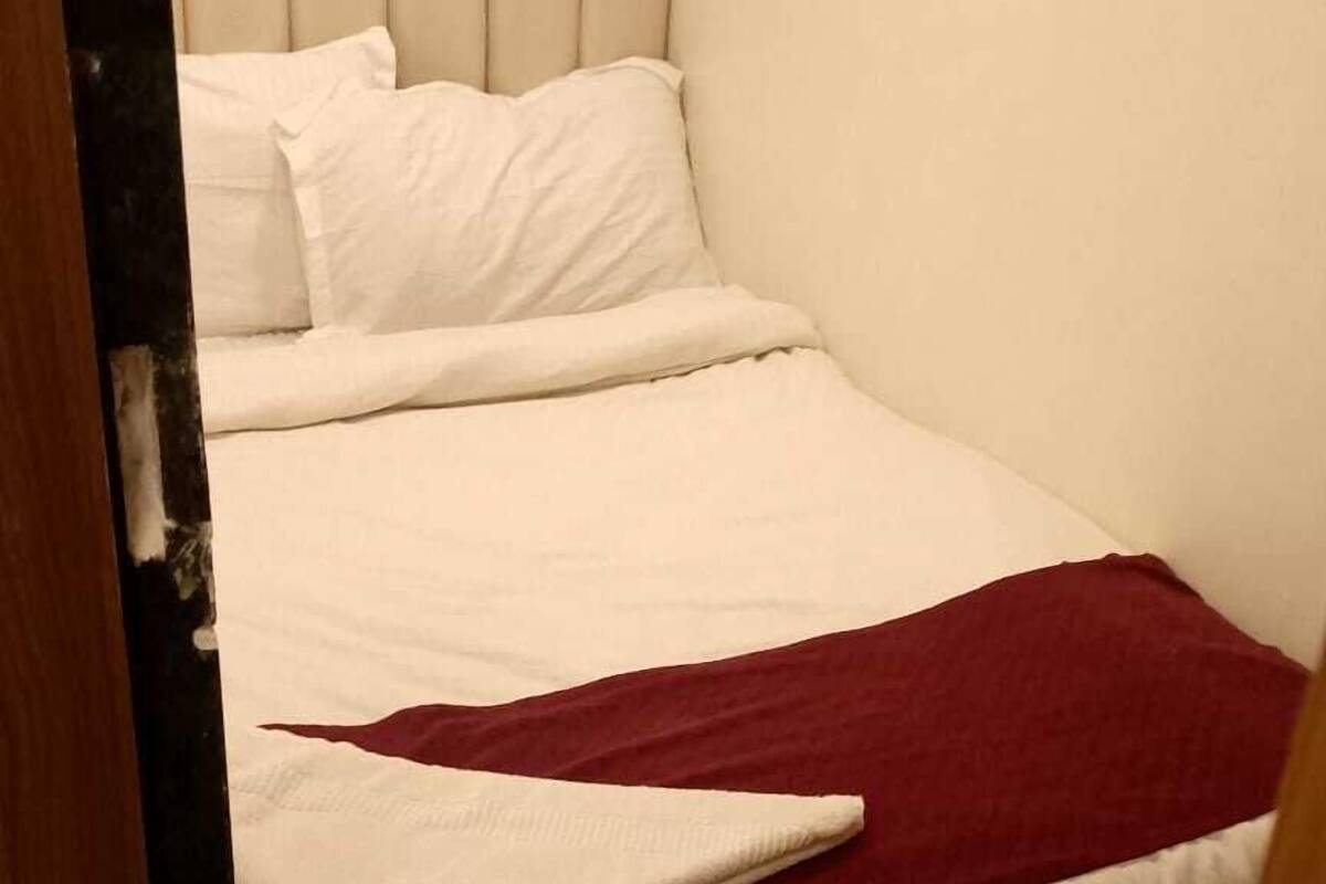 A single bed with white bedding and a red blanket, a wooden headboard, and a marble-patterned floor.