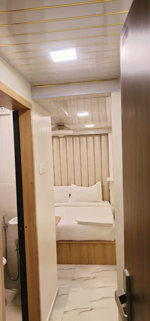 A narrow hallway leading to a bedroom with a bed, a window with blinds, and a shower area.