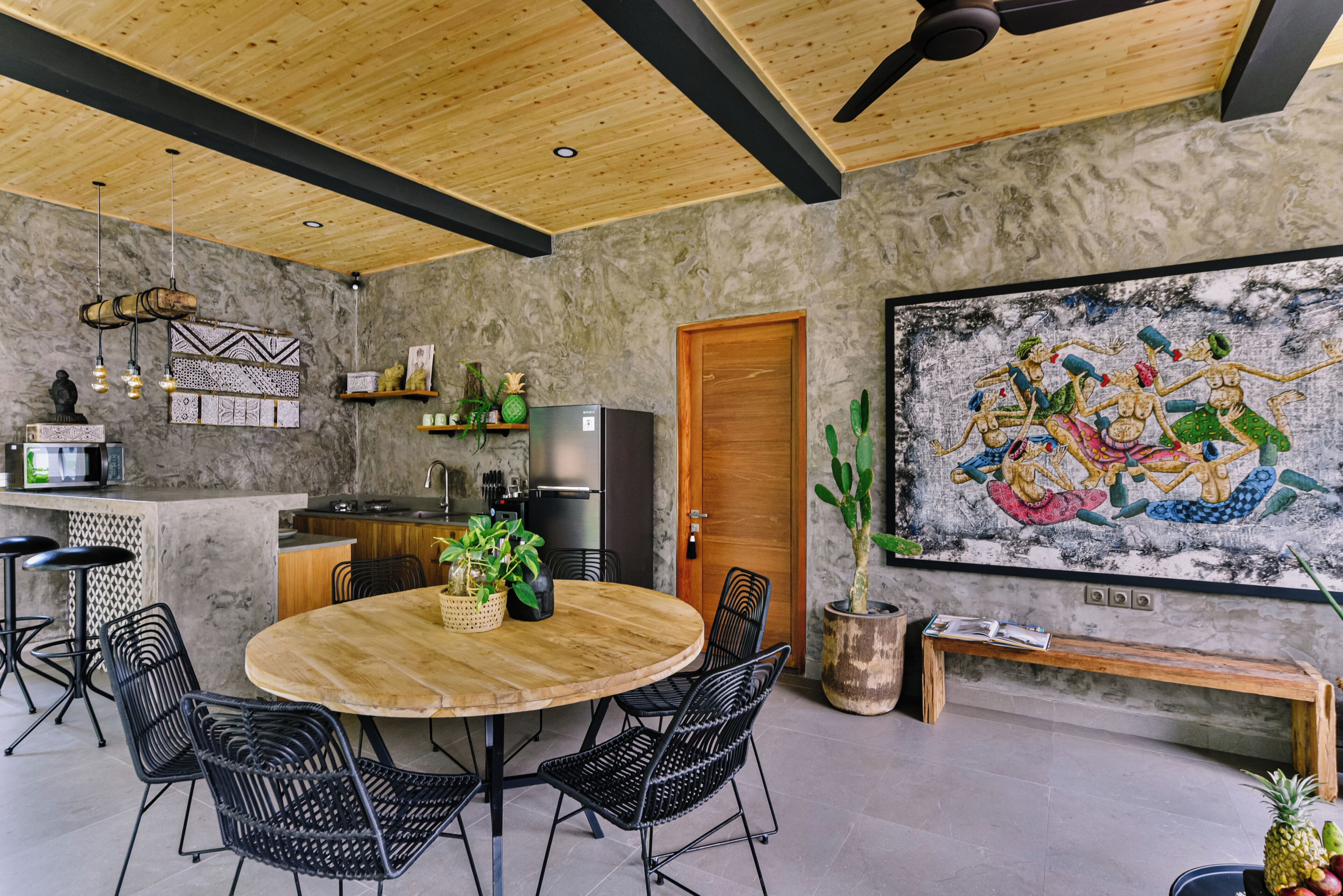 A modern kitchen with a wooden ceiling, a dining area with a round table and chairs, a refrigerator, and a large mural on the wall.